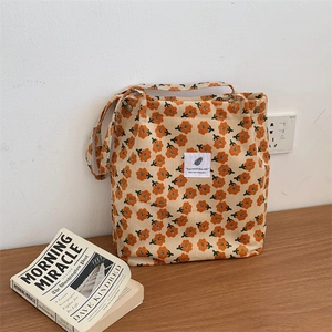 Close-up of corduroy shoulder bag with orange floral print and snap button on wood table