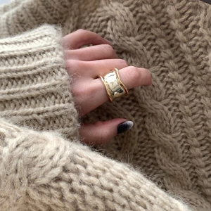 Irregular wide concave gold ring with a polished finish shown on an index finger