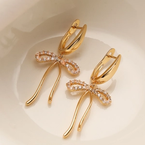 Exquisite gold bow earrings with pavé zircons and dangling tassels on a white background