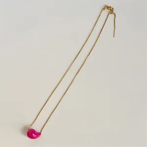Detail of adjustable gold box chain with a pink glazed bean pendant on white surface