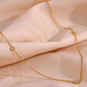 Macro view of dainty gold chain with micro-pave crystal ball on soft pink silk fabric