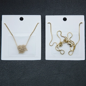 Golden box chain and cross chain necklaces on white display cards over black leather
