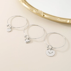 Detailed view of silver stainless steel bangles with heart and medal charms on beige background