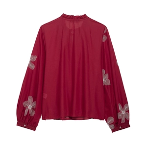 Detail of white floral embroidery on a raspberry red long sleeve blouse with ruffles