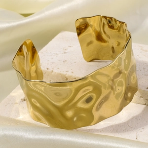 Detail of wide gold cuff bracelet with hammered texture on natural stone and silk