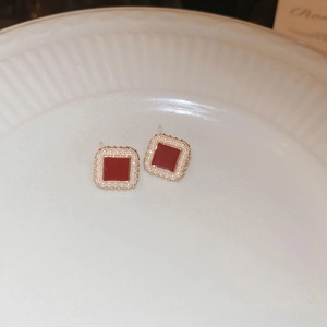 Vue rapprochée de boucles d'oreilles carrées dorées avec émail rouge et perles sur céramique