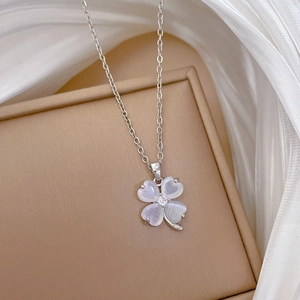 Macro detail of clover necklace with white opal stone and diamond on silk fabric