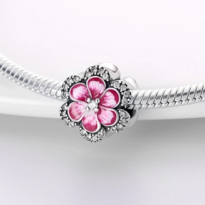 Detalle macro del dije de girasol con esmalte rosa y circonitas en pulsera de serpiente