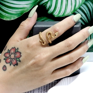 Nahaufnahme des goldenen Schlangenrings mit Schuppentextur an einem Finger mit Blatt