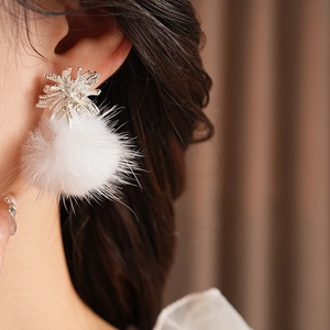 Close-up of a silver snowflake earring with a white fuzzy pompom on a female model