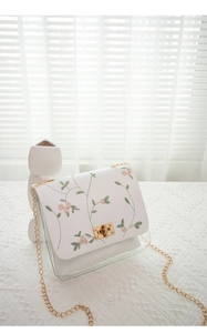 Detail of floral embroidery on white flap with clear body and gold chain strap