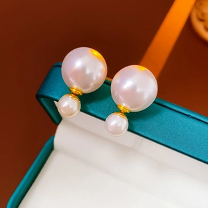 Macro view of double-sided pearl earrings with gold base on a green jewelry box