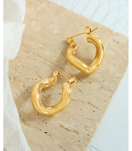 Macro shot of 18k gold plated geometric twisted hoop earrings on beige travertine stone