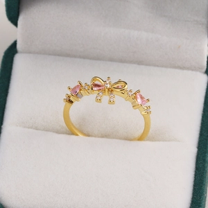 Détail d'une bague nœud dorée avec zircons cœurs roses présentée dans un écrin à bijoux