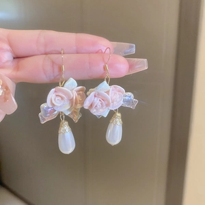 Close-up of pink ceramic rose earring with teardrop pearl and golden hook detail