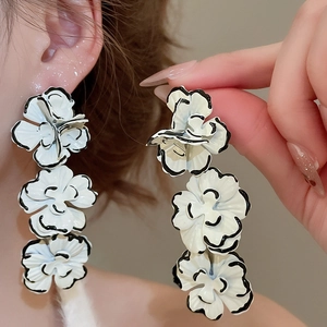 Close-up of three-tiered white flower drop earrings with elegant black painted edges