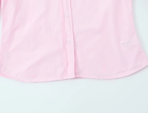 Close-up of light pink poplin shirt hem showing white buttons and woven texture