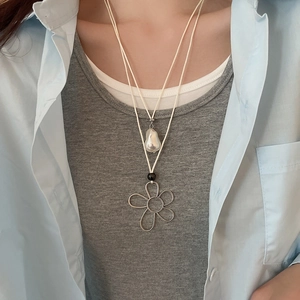 Detail of a layered necklace with baroque pearl and wire-wrapped floral pendant on a model