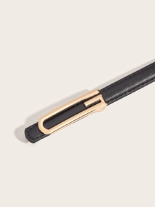 Close-up of black leather belt with polished gold rectangular metal buckle on beige background