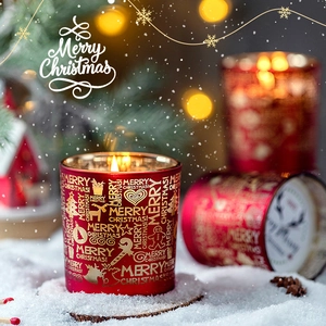 Weihnachtsduftkerze im roten Glas mit goldenen Motiven in einer verschneiten Kulisse