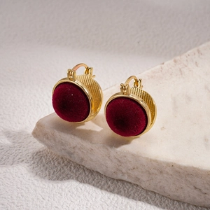 Detail of vintage gold textured earrings with burgundy flocking on a stone surface