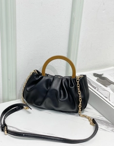 Detail of black ruched cloud bag featuring a wooden handle and golden chain strap