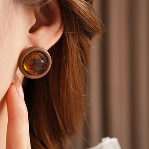 Close-up of amber resin round stud earring on ear with matte metal base detailing
