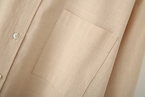 Close-up of beige linen shirt featuring a square pocket and shell-textured button details