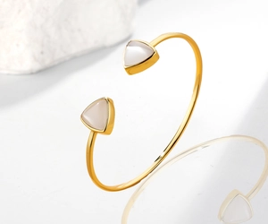 Close-up of a gold open cuff bracelet with triangular opal stones on marble background