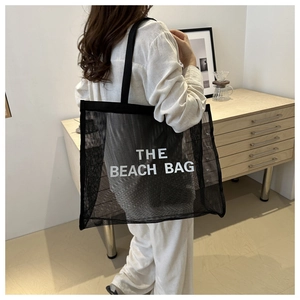 Detail of a black mesh tote bag with THE BEACH BAG print, showing large capacity and handles