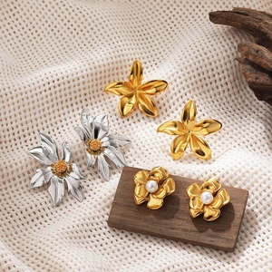 Flat lay of 18k gold flower earrings with pearls and stainless steel sunflower studs