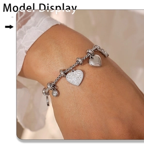 Macro detail of silver heart charm bracelet with zircon inlays on a model's wrist