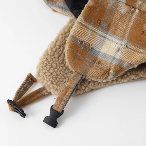 Detail of winter trapper hat featuring brown plaid fabric and warm beige faux fleece lining