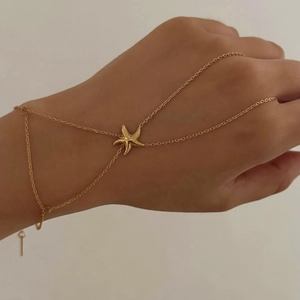 Gold starfish hand back chain with ring attached, worn by a model against a plain wall
