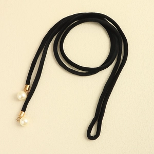 Detail of minimalist black velvet dress belt with golden metal caps and white pearls