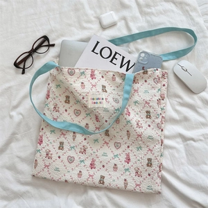 Flat lay of a beige floral canvas tote bag with blue straps and lifestyle accessories