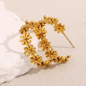 Vue macro de boucles d'oreilles créoles dorées en forme de C avec motif floral ajouré