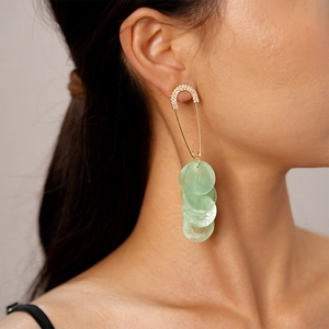 Close-up of dangling green shell discs and rhinestone safety pin earrings worn by a model