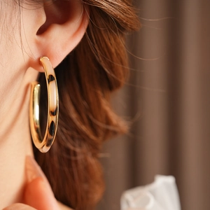 Close-up of a large C-shaped tortoiseshell resin earring worn by a model with gold interior
