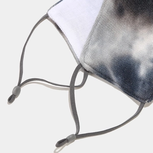 Detail of tie-dye protective mask featuring adjustable grey ear loops and soft white lining
