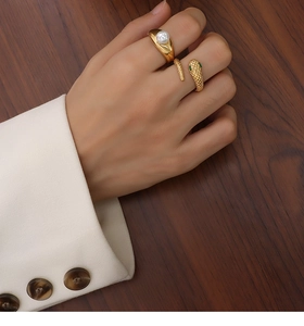 Detail of 18k gold plated snake ring and pearl ring set on model hand against dark wood