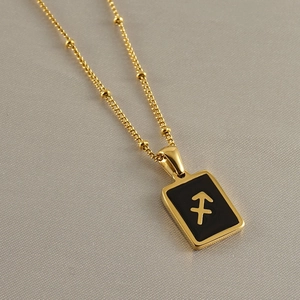 Close-up of golden square pendant with black enamel Sagittarius zodiac sign