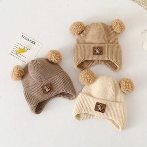 Winter baby knit hats with dinosaur patches and double pom-poms in three warm earth tones