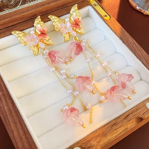 Nahaufnahme goldener Schmetterlingsohrringe mit rosa Blumen und Perlenketten-Quasten