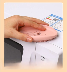 Pink cat-paw silicone cleaning brush scrubbing the edge of a white kitchen microwave