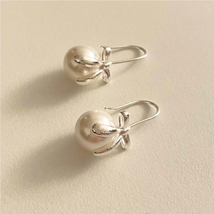 Close-up of 925 sterling silver bowknot earrings with white pearls on a beige surface