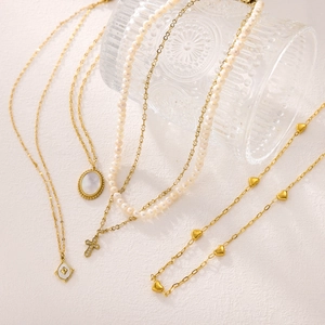 Detailed display of assorted gold necklaces with pearl, cross, heart and shell pendants