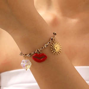 Close-up of Bohemian woven bracelet with gold sun charm and red lip pendant