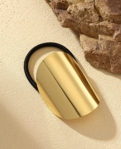 Detail of a polished gold oval metal hair cuff with a black elastic hair tie on a stone