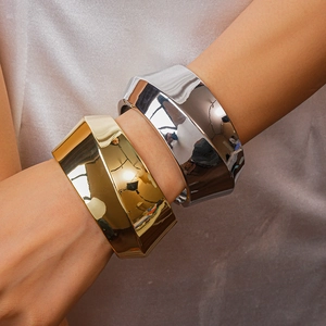 Detailed view of polished gold and silver geometric wide bangles on a model wrist
